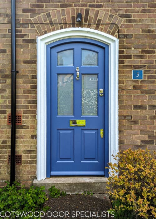 arched Georgian front door painted blue fitted into a brick house. Door and frame are both Accoya wood and painted blue. Banham high security locks. All door hardware polished chrome. Sandblasted glass with Clear inset border, double glazed