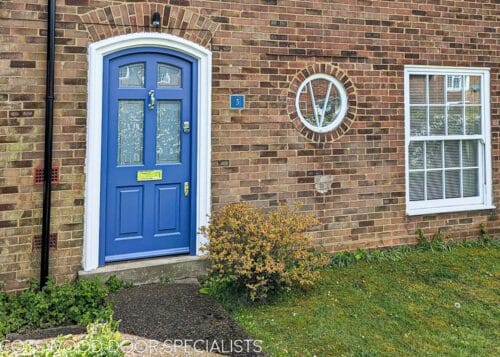 arched Georgian front door painted blue fitted into a brick house. Door and frame are both Accoya wood and painted blue. Banham high security locks. All door hardware polished chrome. Sandblasted glass with Clear inset border, double glazed