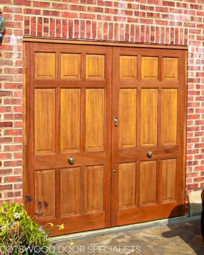 Panelled garage doors. Wooden garage doors featuring 9 panells in each doors. Fitted into a new door frame into a red brick garage. Bespoke design of doors. Fitted with high quaility brass door furniture and secure locks