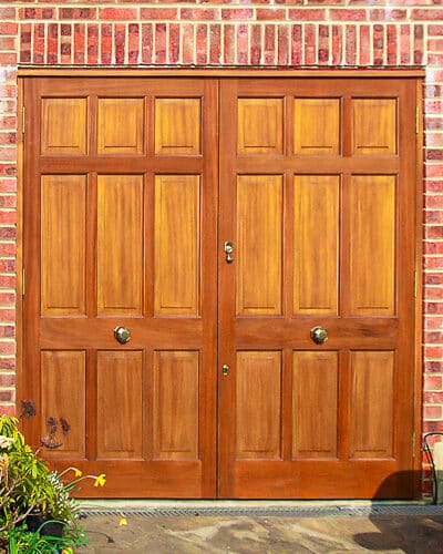Panelled garage doors. Wooden garage doors featuring 9 panells in each doors. Fitted into a new door frame into a red brick garage. Bespoke design of doors. Fitted with high quaility brass door furniture and secure locks
