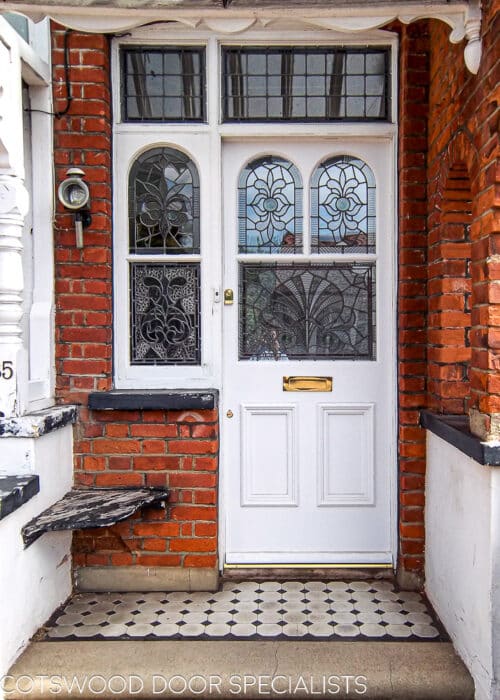 Traditional Edwardian front door. Door is painted white and the frame is painted white too. Fitted into a London red brick home. Door is a replica of the orginal design with shaped glass matching the orginal door frame. The glass is ornated leaded stained glass featuring rondels and different textures. Door has decorative mouldings and brass door furniture.