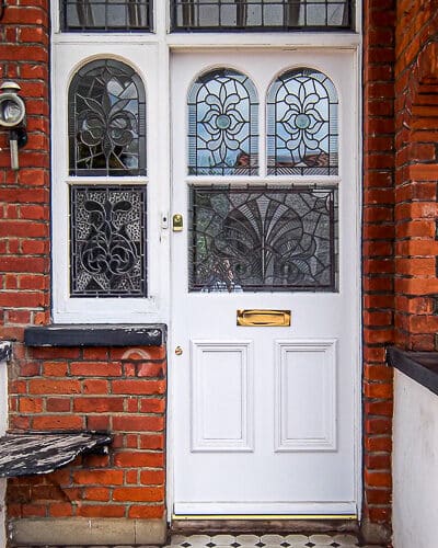 Traditional Edwardian front door. Door is painted white and the frame is painted white too. Fitted into a London red brick home. Door is a replica of the orginal design with shaped glass matching the orginal door frame. The glass is ornated leaded stained glass featuring rondels and different textures. Door has decorative mouldings and brass door furniture.