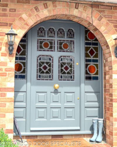 grey painted Victorian front door and double sidelight frame fitted in london. door has vibrant geometric stained glass. laminated stained glass. Draught proofed and insurance rated locks fitted. door furniture is polished brass. bright colours flood light into hallway though glass. Door is of an intricate design with 8 panes of glass, some of which are shaped