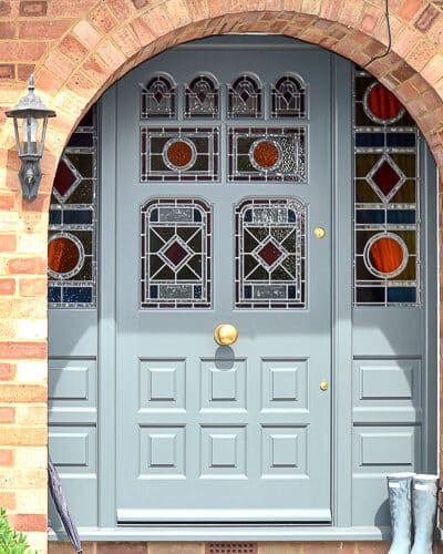 grey painted Victorian front door and double sidelight frame fitted in london. door has vibrant geometric stained glass. laminated stained glass. Draught proofed and insurance rated locks fitted. door furniture is polished brass. bright colours flood light into hallway though glass. Door is of an intricate design with 8 panes of glass, some of which are shaped
