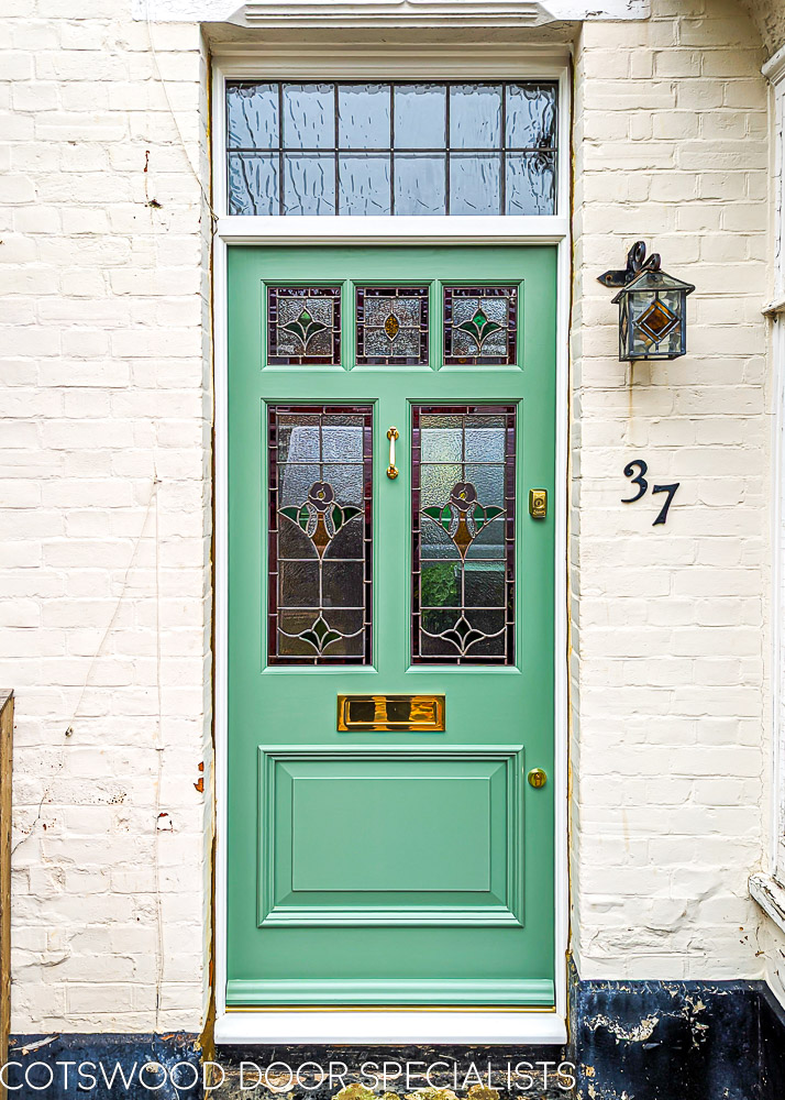 London style Edwardian door. A london style edwardian front door with stained glass. Door is painted green and is fitted into a frame with an overpanel of glass. The door is fitted into a london home with a bay window. Door has five pieces of glass, all square or rectangular. The glass is stained glass made from indivially cut pieces of glass. Stained glass design features a flower taken from original windows. High secuirty brass locks