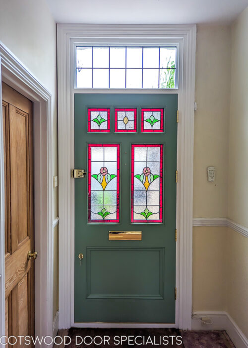 London style Edwardian door. A london style edwardian front door with stained glass. Door is painted green and is fitted into a frame with an overpanel of glass. The door is fitted into a london home with a bay window. Door has five pieces of glass, all square or rectangular. The glass is stained glass made from indivially cut pieces of glass. Stained glass design features a flower taken from original windows. High secuirty brass locks. Hallway photo showcasing stained glass and architraves