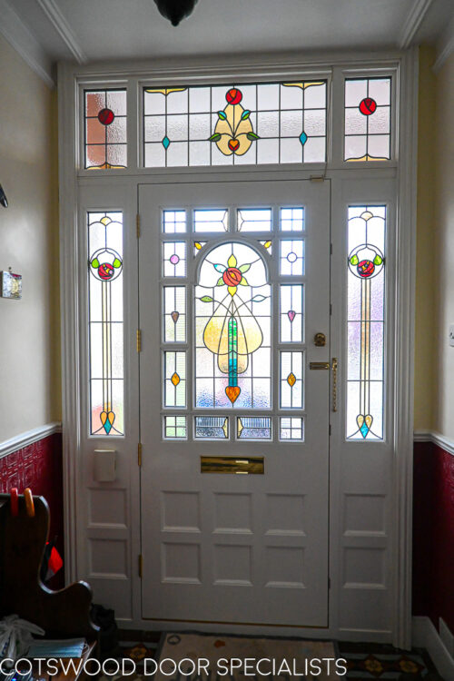 ornamental Edwardian front door with stained glass. A decorative 17 light Edwardian front door with decorative features such as a shelf and dentil block and an apron of which the letterplate is fixed too. The frame is a large frame with sidelights and glazing above the door. The door frame is very ornamental with pilasters (detailed moulding forming columns each side of the door) supporting a decorative transom with detailed mouldings and a dentil block. The stained glass is a art nouveau design featuring roses. door and frame are a replica of the orignal Edwardian joinery. Handmade in Accoya wood and fitted with multipoint locking. Internal picture of stained glass