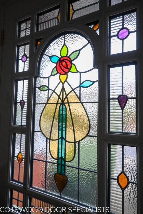 ornamental Edwardian front door with stained glass. A decorative 17 light Edwardian front door with decorative features such as a shelf and dentil block and an apron of which the letterplate is fixed too. The frame is a large frame with sidelights and glazing above the door. The door frame is very ornamental with pilasters (detailed moulding forming columns each side of the door) supporting a decorative transom with detailed mouldings and a dentil block. The stained glass is a art nouveau design featuring roses. door and frame are a replica of the orignal Edwardian joinery. Handmade in Accoya wood and fitted with multipoint locking. Internal picture of stained glass