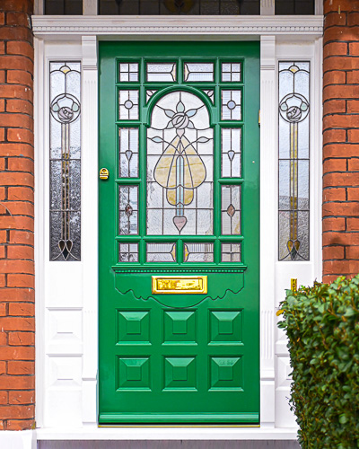 ornamental Edwardian front door with stained glass. A decorative 17 light Edwardian front door with decorative features such as a shelf and dentil block and an apron of which the letterplate is fixed too. The frame is a large frame with sidelights and glazing above the door. The door frame is very ornamental with pilasters (detailed moulding forming columns each side of the door) supporting a decorative transom with detailed mouldings and a dentil block. The stained glass is a art nouveau design featuring roses. door and frame are a replica of the orignal Edwardian joinery. Handmade in Accoya wood and fitted with multipoint locking