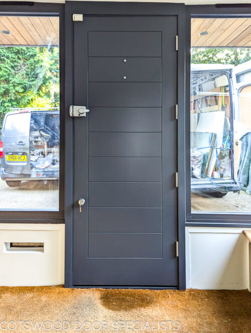 Yellow Contemporary front door. New accoya wooden door fitted into a new wooden frame. Door is contemporary in style with lots of glazing surrounding the door. The frame is painted grey and the door a bright yellow. The door is solid wood with no glass and horizontal wooden panels. Satin chrome door furniture and door locks. Interior photo of grey door